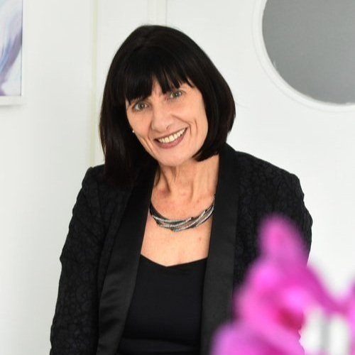 A woman with a dark bob wearing black, photographed indoors against a pale wall